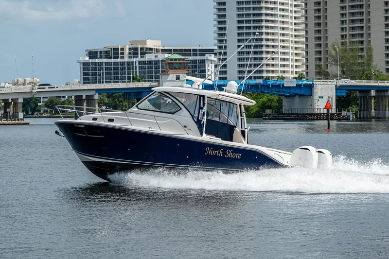 Slide: The Image of Pursuit boat "North Shore" cruising on water near urban bridge and buildings. - 20