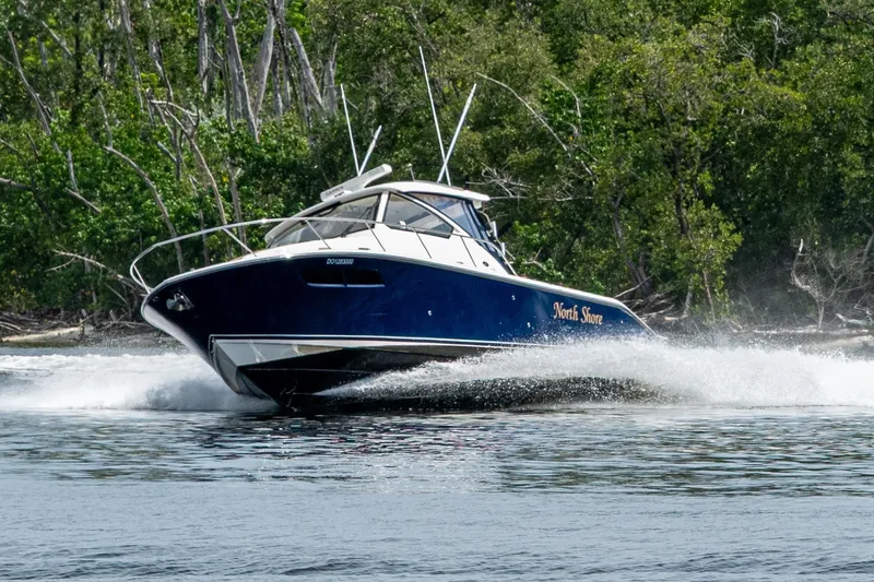 Slide: The Image of Pursuit boat "North Shore" cruising swiftly on water near lush green forest. - 58