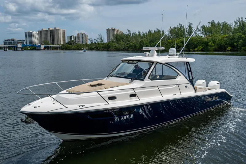 Slide: The Image of Pursuit boat cruising on a river with city skyline and trees in the background. - 59