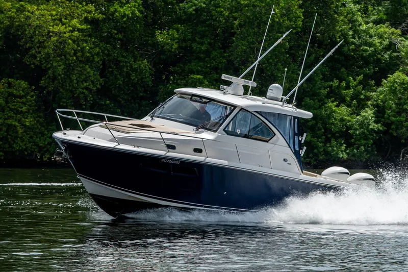 Slide: The Image of Pursuit boat cruising on water with lush green trees in the background. - 9