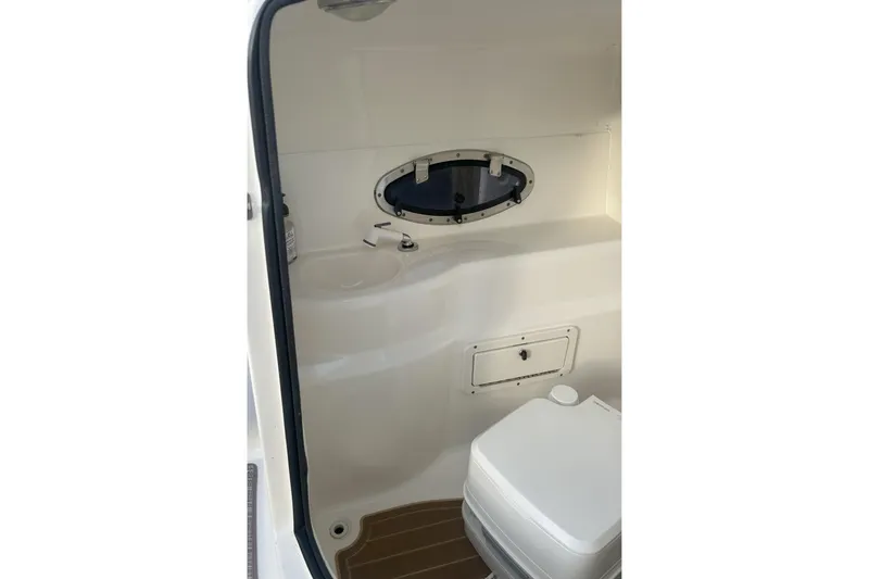 Slide: The Image of 2018 NauticStar 243DC Sport Deck interior with compact marine toilet and porthole. - 19