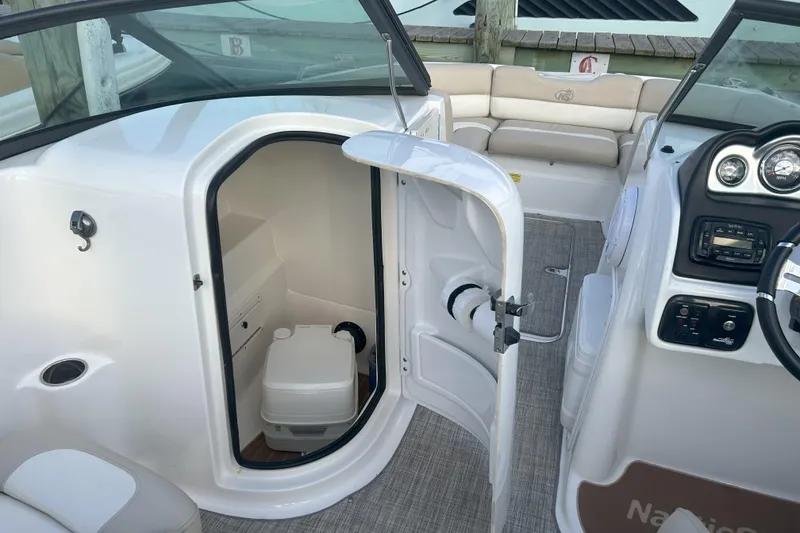 Slide: The Image of 2018 NauticStar 243DC Sport Deck boat interior with open restroom door and dashboard view. - 22