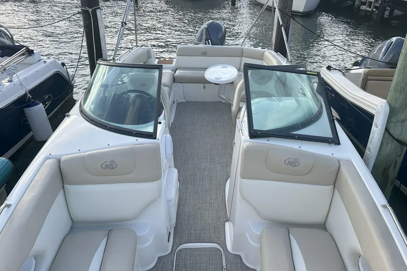 Slide: The Image of 2018 NauticStar 243DC Sport Deck boat interior with seating and table, docked by the water. - 5