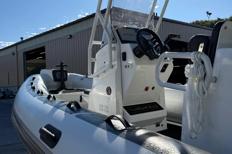 Slide: The Image of 2024 Highfield Sport 560 boat interior with steering wheel and rope, docked near a warehouse. - 14