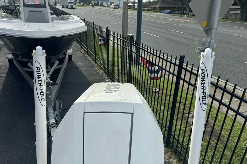 Slide: The Image of 2026 Ranger 2510 Bay boat with Power-Pole anchors, parked near a roadside fence. - 13