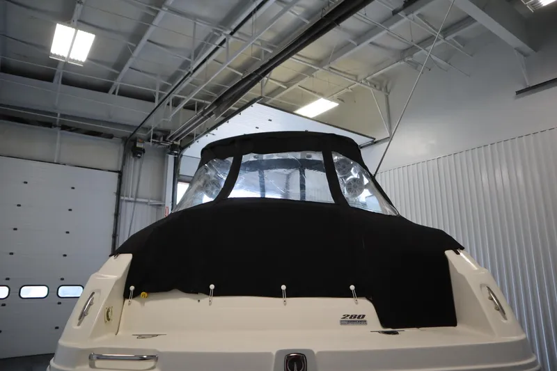 Slide: The Image of 2013 Sea Ray 280 Sundancer boat in indoor storage, rear view with black cover. - 86