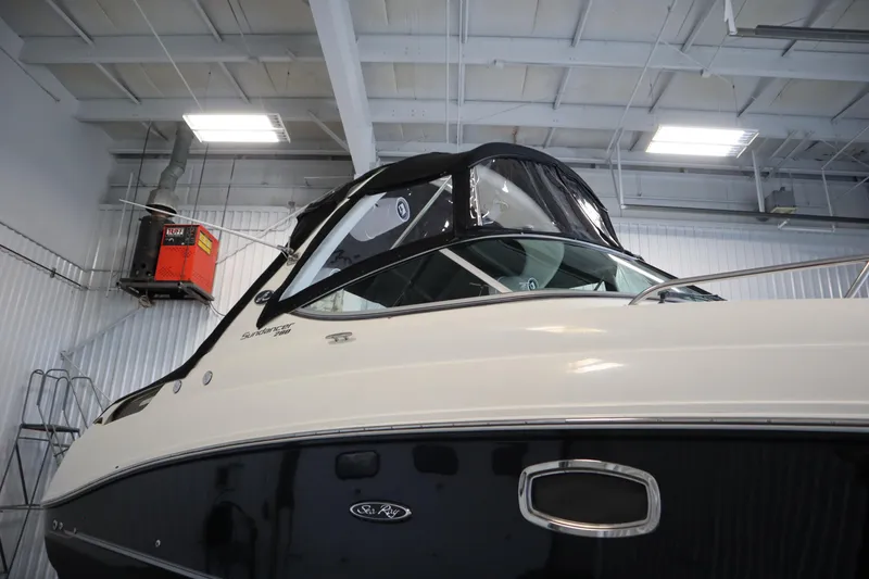 Slide: The Image of 2013 Sea Ray 280 Sundancer boat in indoor storage, showcasing sleek design and black canopy. - 87