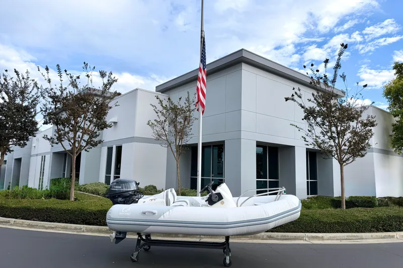 Slide: The Image of 2003 Zodiac Yachtline 340DL boat on trailer, parked outside modern building with American flag. - 18