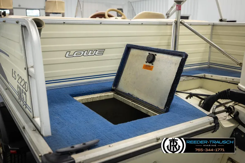 Slide: The Image of 1998 Lowe LS 2220 boat with open storage compartment, blue carpet, and visible branding. - 23