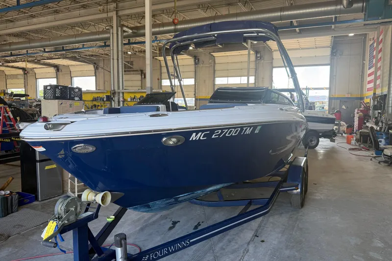 The Image of 2011 FOURWINNS 210 boat in a workshop, blue hull, on a trailer. - 1