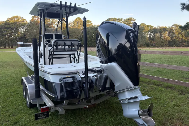 Slide: The Image of 2022 BlackJack 256 Bay boat on trailer, parked on grass with trees in background. - 6