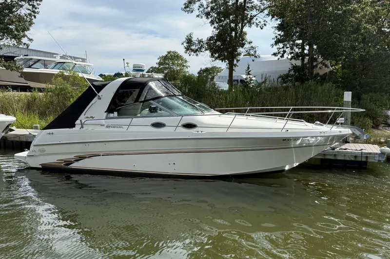 Slide: The Image of 1998 Sea Ray 290 Sundancer boat docked on calm water, surrounded by greenery. - 2