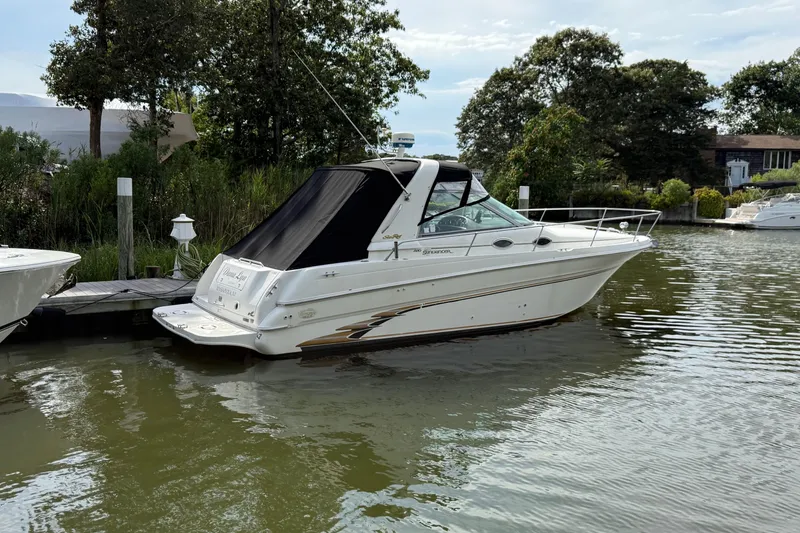 Slide: The Image of 1998 Sea Ray 290 Sundancer docked on a calm waterway, surrounded by lush greenery. - 4