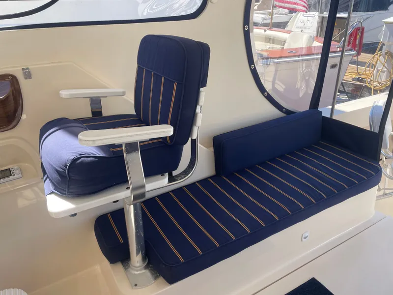 Slide: The Image of 2005 Mainship Pilot 30-II interior with blue striped seating and round window view. - 16