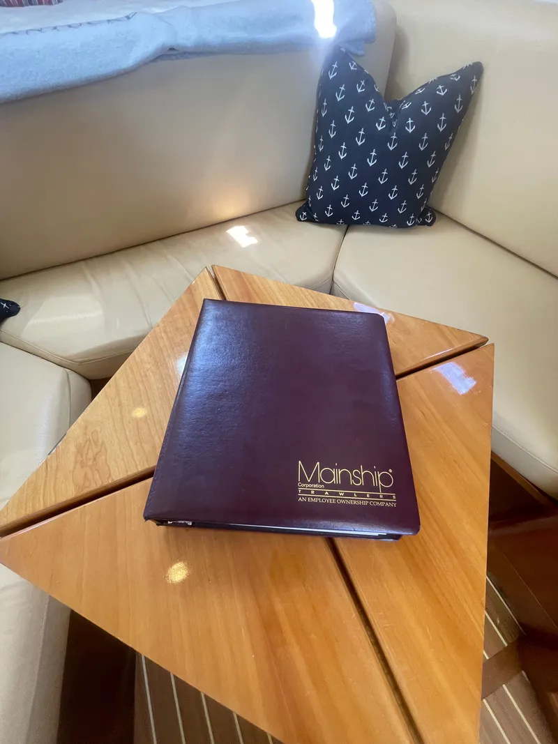 Slide: The Image of 2005 Mainship Pilot 30-II interior with a triangular wooden table and anchor-themed pillow. - 45