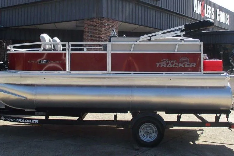 The Image of 2026 Sun Tracker Bass Buggy® 16 XL Select pontoon boat on trailer, parked outside dealership. - 1