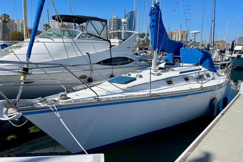 Slide: The Image of 1984 Hunter 34 sailboat docked in marina, blue sail covers, clear sky background. - 2