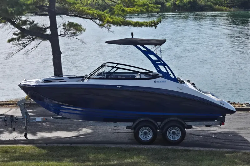 The Image of 2020 Yamaha AR210 boat on trailer by a lake, under tree shade. - 0