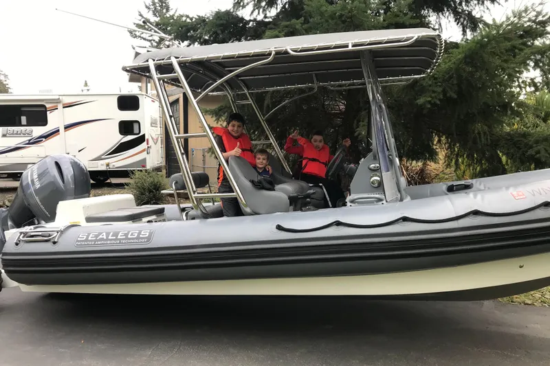 Slide: The Image of 2013 Sealegs 7.7 RIB boat with passengers, parked near a camper and trees. - 5