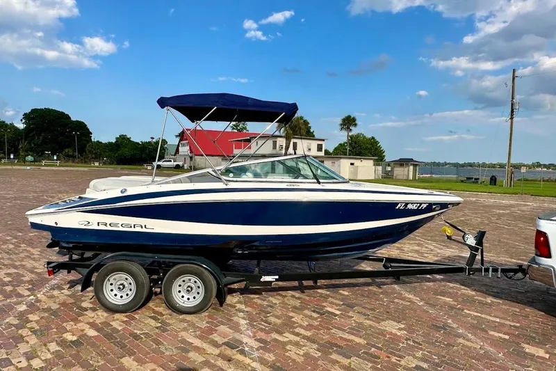 The Image of 2012 Regal 2100 boat on trailer, parked on brick pavement under blue sky. - 1