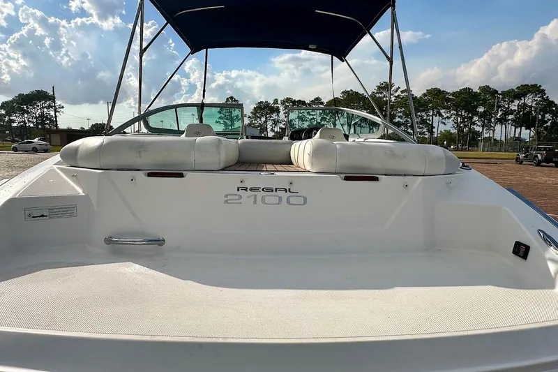 Slide: The Image of 2012 Regal 2100 boat with canopy, parked outdoors under a partly cloudy sky. - 12