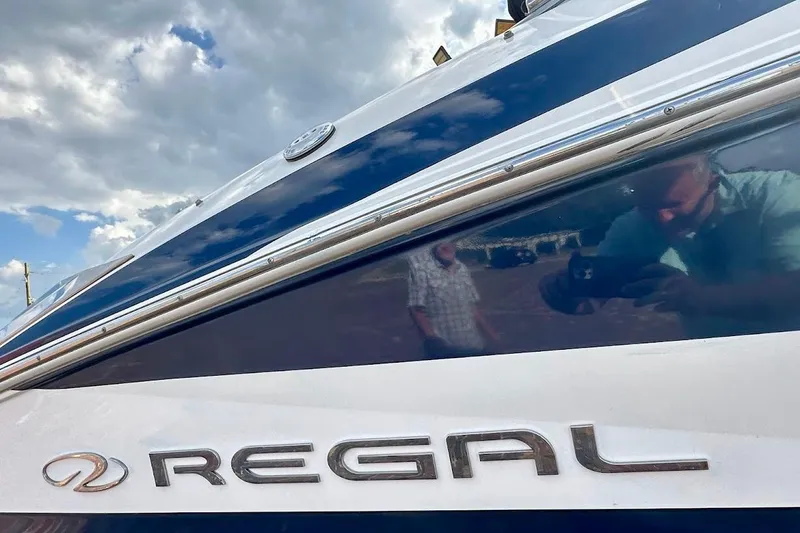 Slide: The Image of 2012 Regal 2100 boat with reflective surface and logo under cloudy sky. - 14