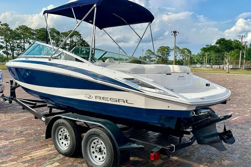 Slide: The Image of 2012 Regal 2100 boat on trailer, blue and white design, parked outdoors. - 6