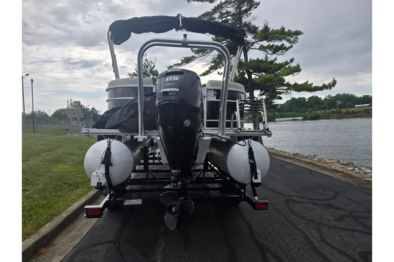 Slide: The Image of 2023 Starcraft EX 22 R pontoon boat with Mercury outboard motor, parked by a riverside. - 2
