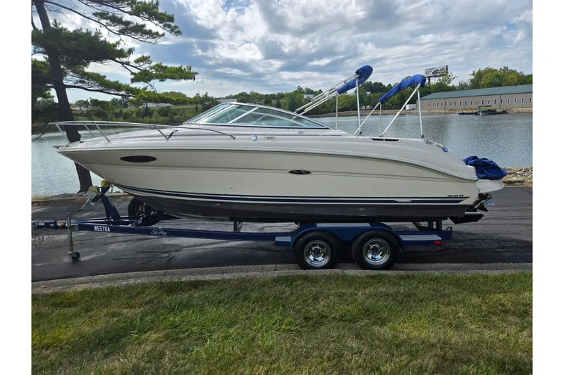 Slide: The Image of 2002 Sea Ray 225 Weekender boat on trailer by a lake, under cloudy sky. - 9