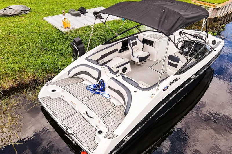 Slide: The Image of 2023 Yamaha Boats SX195 with black canopy, docked on calm water. - 20
