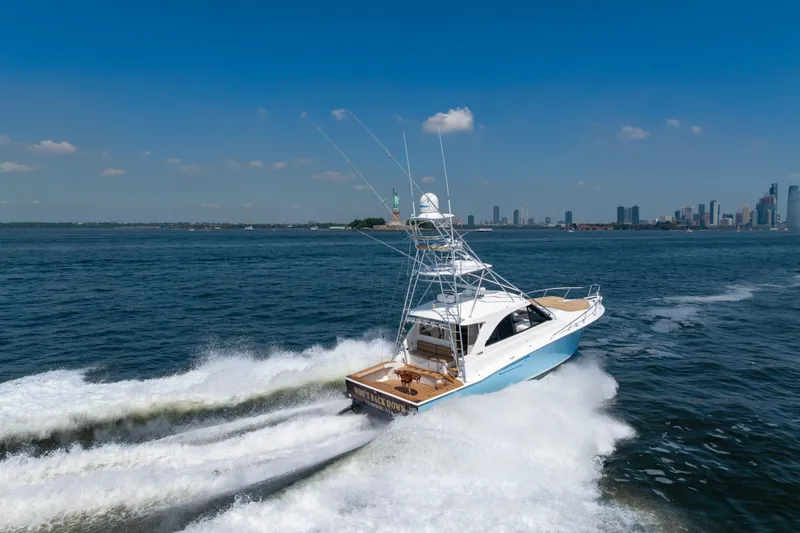 Slide: The Image of 2012 Cabo 44 Hardtop Express yacht cruising near city skyline on a sunny day. - 27