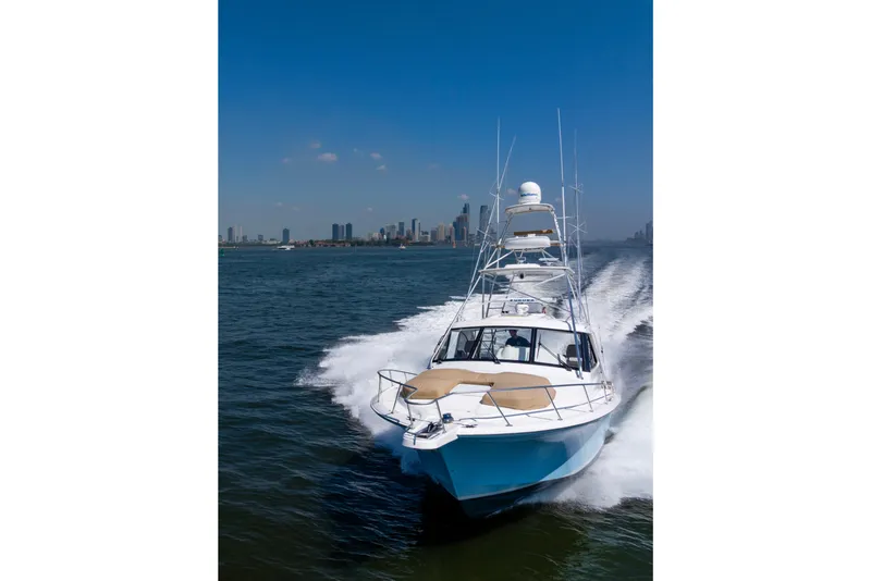 Slide: The Image of 2012 Cabo 44 Hardtop Express yacht cruising on open water with city skyline backdrop. - 29