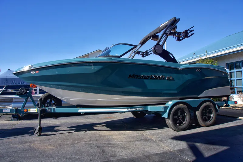 The Image of 2025 MasterCraft NXT20 boat on trailer, parked outdoors under clear blue sky. - 0