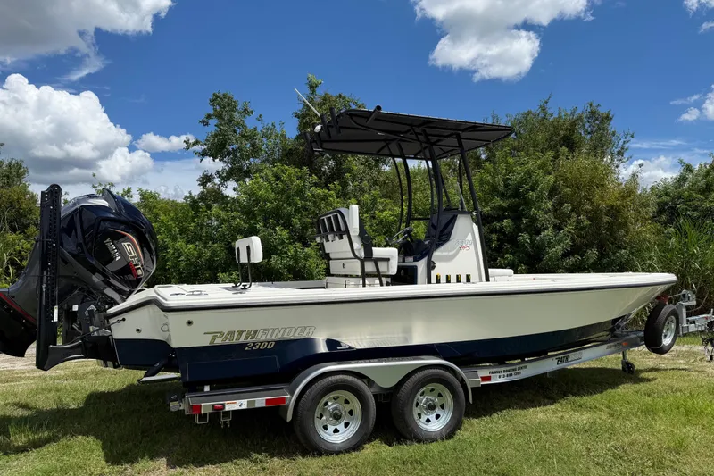 Slide: The Image of 2026 Pathfinder 2300 HPS boat on trailer, parked on grass with trees in background. - 2