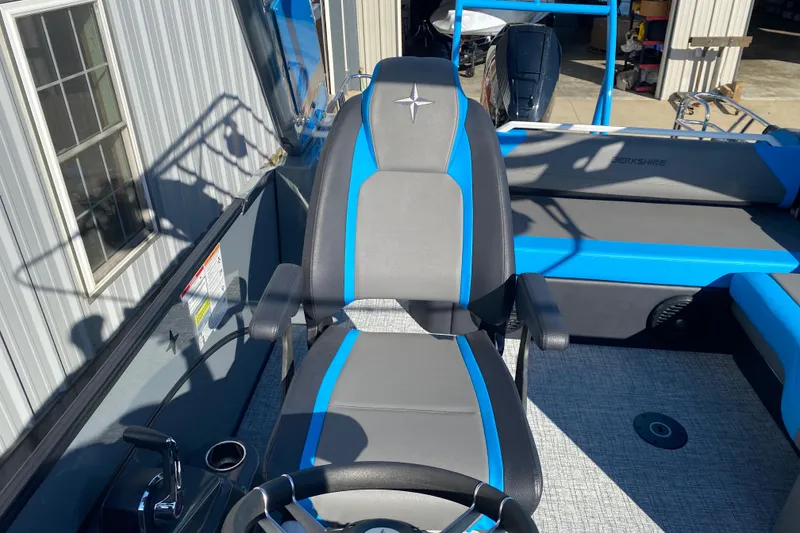 Slide: The Image of 2023 Berkshire 23UL boat interior with blue and gray seating, steering wheel, and controls. - 19