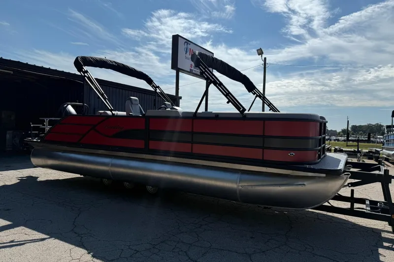 Slide: The Image of 2025 Bentley Pontoons Legacy 243 Swingback, red and black design, parked outdoors under a blue sky. - 4