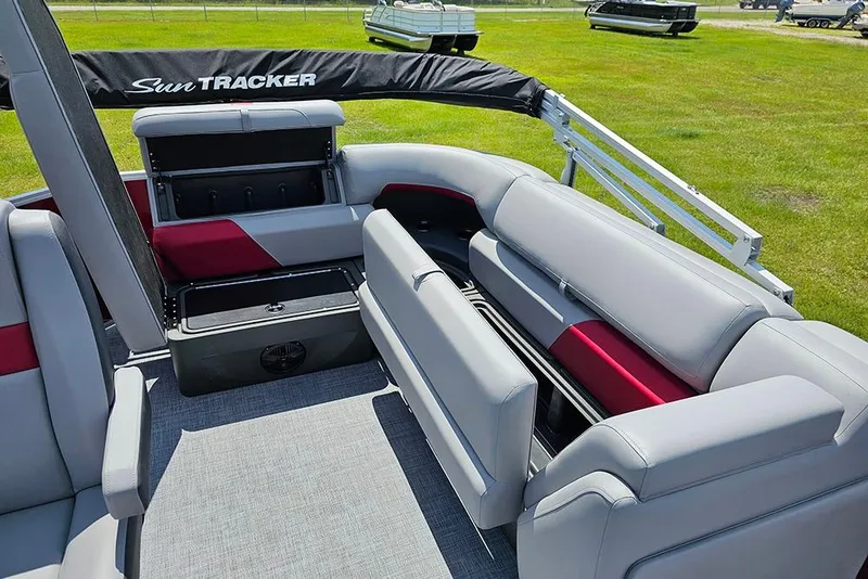 Slide: The Image of 2026 Sun Tracker Party Barge 20 DLX interior with gray and red seating on grassy background. - 13