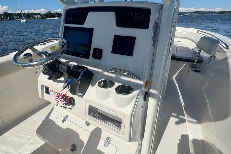 Slide: The Image of 2024 Sailfish 241 CC boat console with steering wheel and navigation screens on a sunny day. - 10