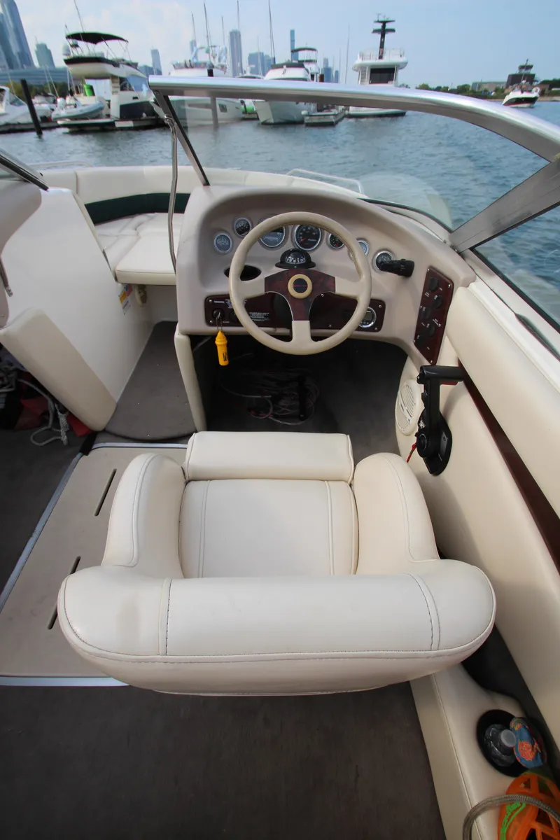 Slide: The Image of 1999 Bryant 182 boat interior with steering wheel and white seating, docked at marina. - 13