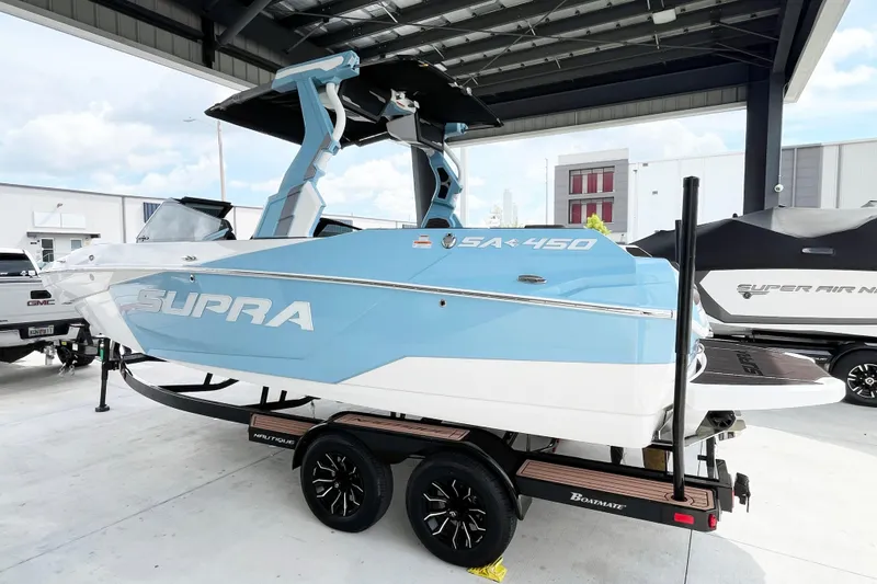Slide: The Image of 2025 Supra SA450 boat in blue and white on a trailer under a canopy. - 2