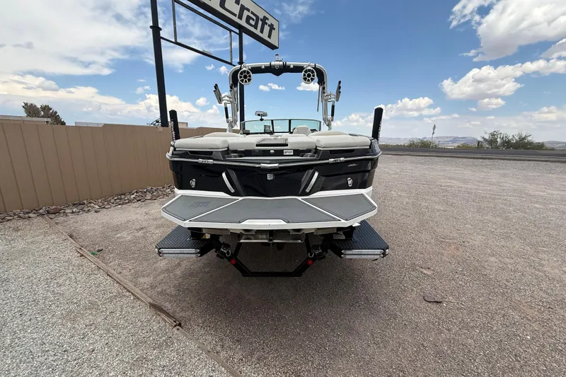 Slide: The Image of 2018 MasterCraft XT25 boat, rear view, parked on gravel under a cloudy sky. - 5