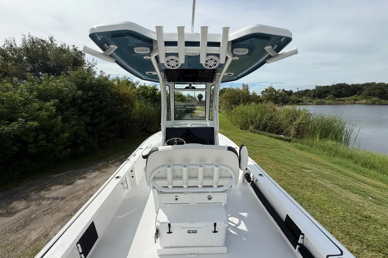 Slide: The Image of 2026 Tidewater 2410 Bay Max boat with T-top, docked near lush greenery and calm water. - 12