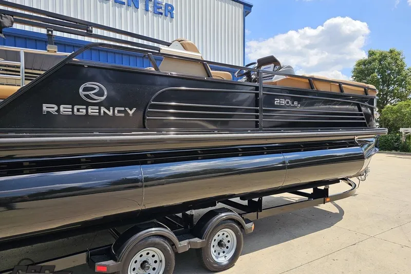 Slide: The Image of 2021 Regency 230 LE3 pontoon boat on trailer, parked outdoors under blue sky. - 13