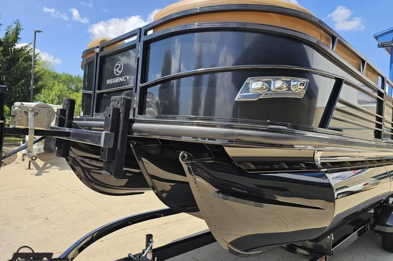 Slide: The Image of 2021 Regency 230 LE3 pontoon boat on trailer, sleek black design under blue sky. - 25