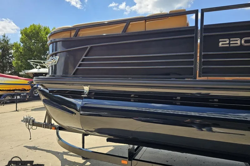 Slide: The Image of 2021 Regency 230 LE3 pontoon boat on trailer, sleek black design under blue sky. - 31