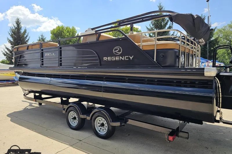 Slide: The Image of 2021 Regency 230 LE3 pontoon boat on trailer, sunny day, trees in background. - 38