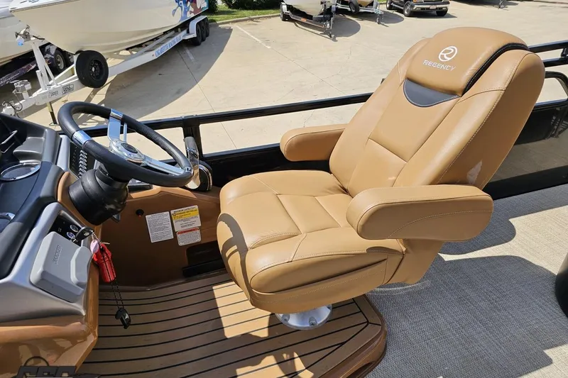 Slide: The Image of Captain's chair on 2021 Regency 230 LE3 boat, featuring tan leather upholstery and steering wheel. - 77