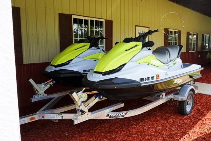 Slide: The Image of Two 2023 Kawasaki Jetski STX 160s on a trailer, parked outside a building. - 1