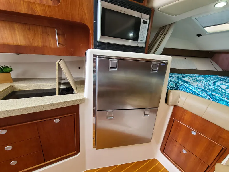 Slide: The Image of 2011 Grady-White Express 360 interior with kitchenette, stainless steel fridge, and cozy sleeping area. - 18