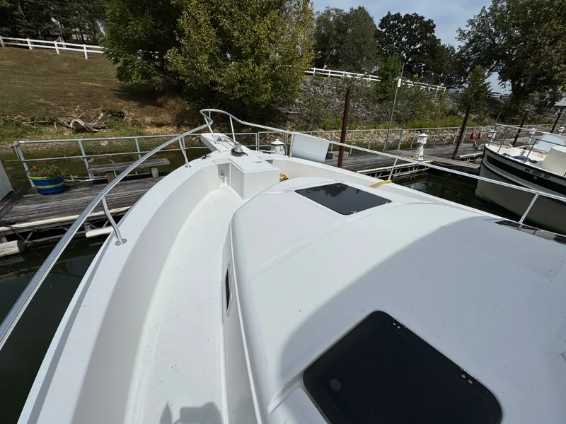 Slide: The Image of 2001 Mainship 390 boat docked, featuring spacious deck and railing, surrounded by greenery. - 12